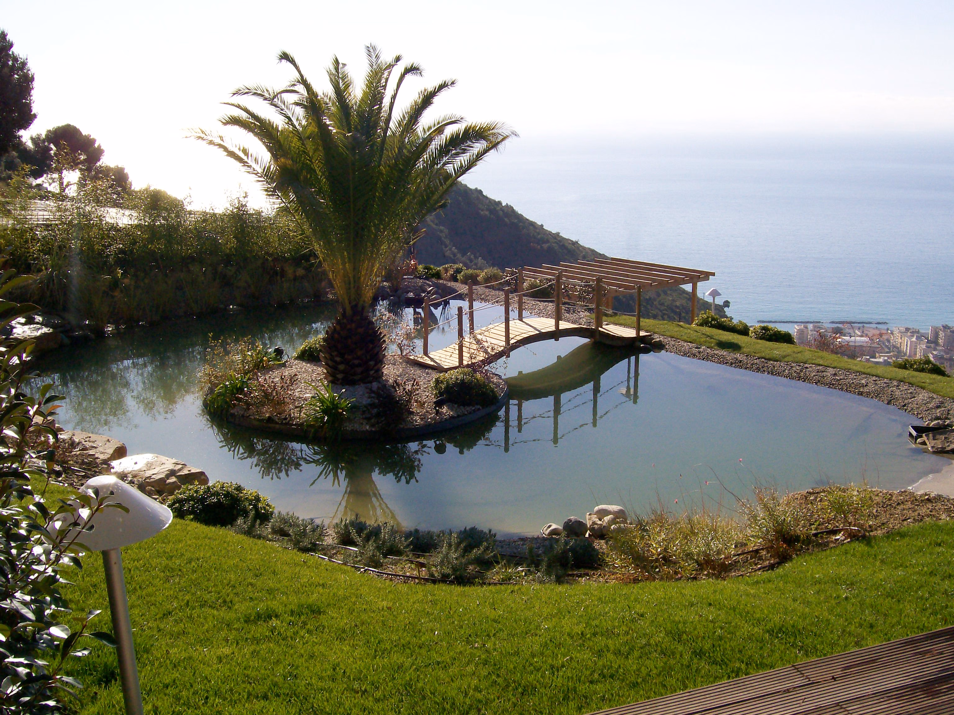 Un biolago con un’isola di palme e un ponte di legno, sopra il mare di Sanremo